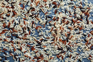 Photo of Brown and other types of rice scattered on color wooden background