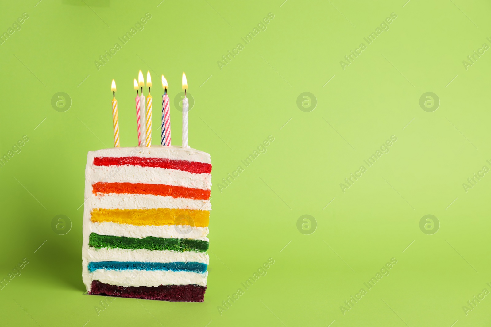 Photo of Slice of delicious rainbow cake with candles on color background