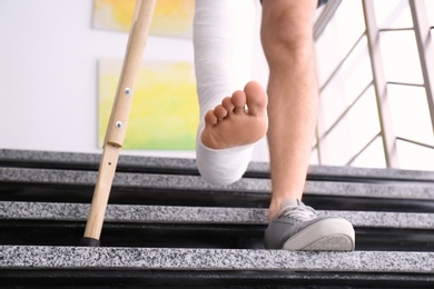 Photo of Young man with crutch and broken leg in cast on stairs