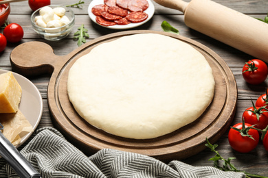 Photo of Dough and fresh ingredients for pepperoni pizza on wooden table