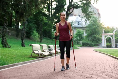 Photo of Young woman practicing Nordic walking with poles outdoors