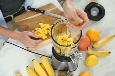Man adding mango into blender with ingredients for smoothie, above view