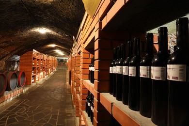 Photo of Beregove, Ukraine - June 23, 2023: Bottles and wooden barrels with alcohol drinks in cellar