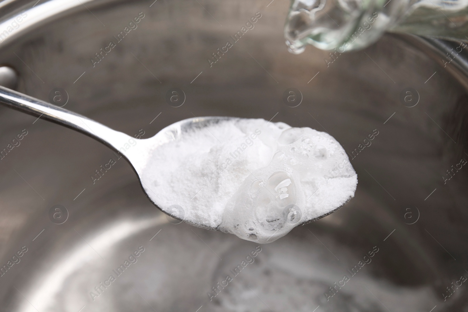 Photo of Pouring vinegar into spoon with baking soda over saucepan, closeup