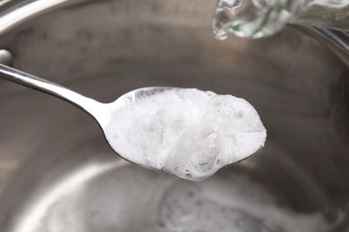 Pouring vinegar into spoon with baking soda over saucepan, closeup