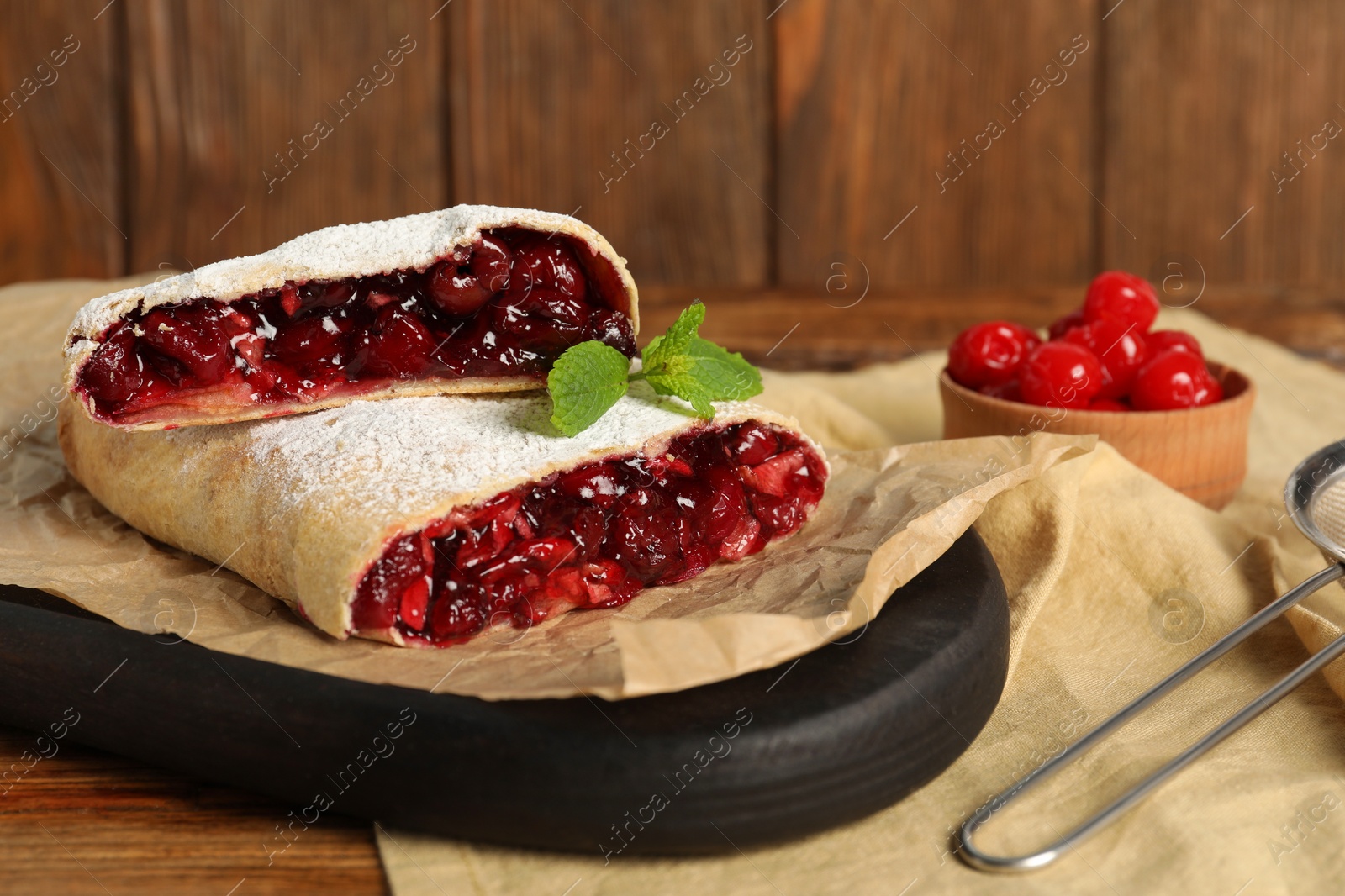 Photo of Delicious strudel with cherries on wooden table, closeup