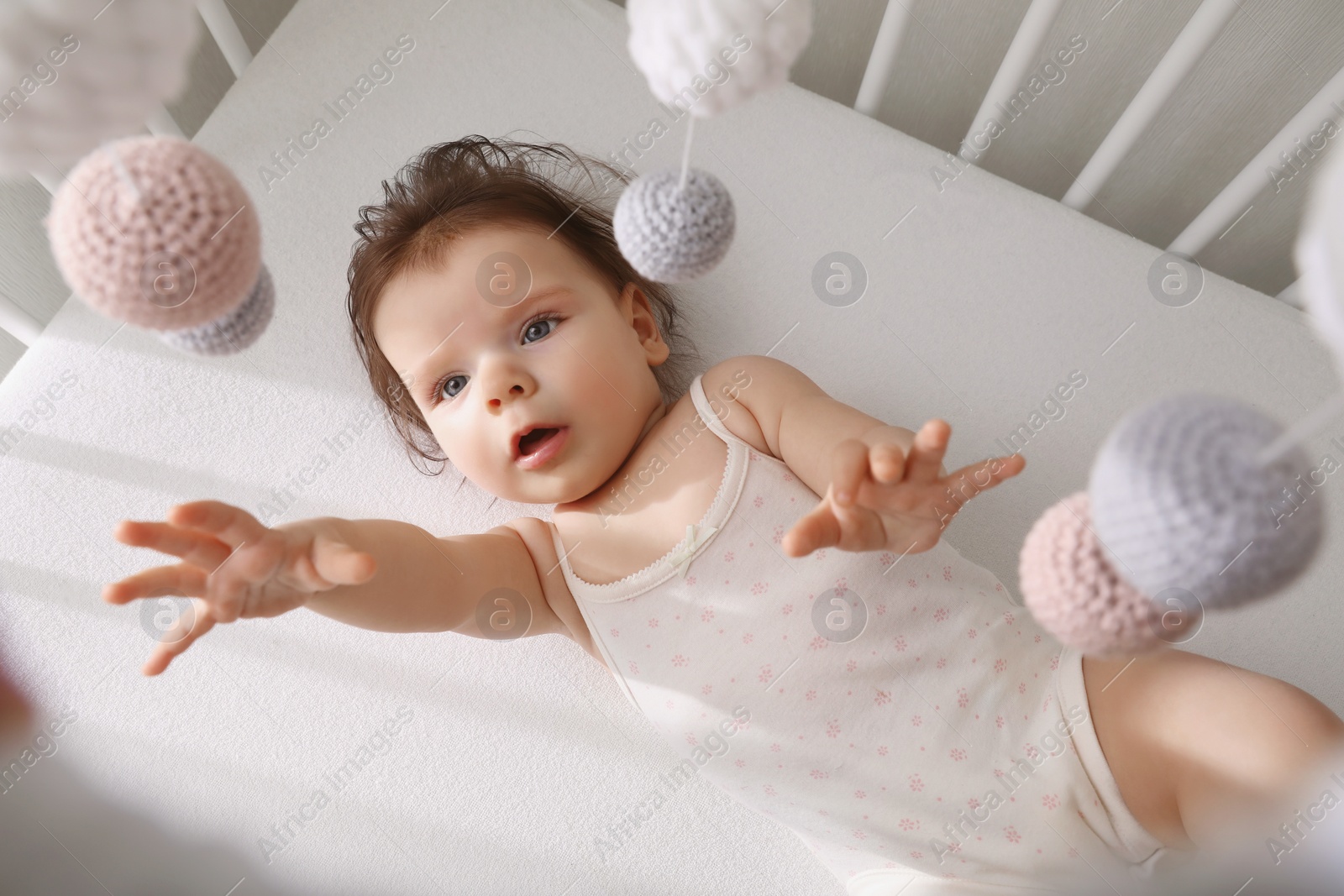 Photo of Cute little baby looking at hanging mobile in crib, top view