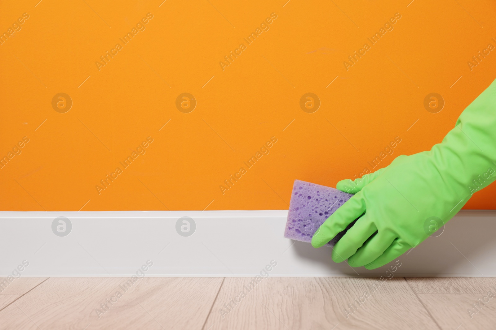 Photo of Woman in protective glove cleaning plinth with sponge indoors, closeup. Space for text