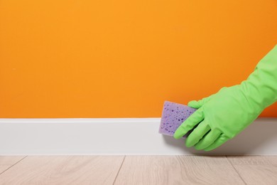 Photo of Woman in protective glove cleaning plinth with sponge indoors, closeup. Space for text