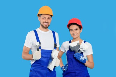 Photo of Professional workers with putty knives in hard hats on light blue background