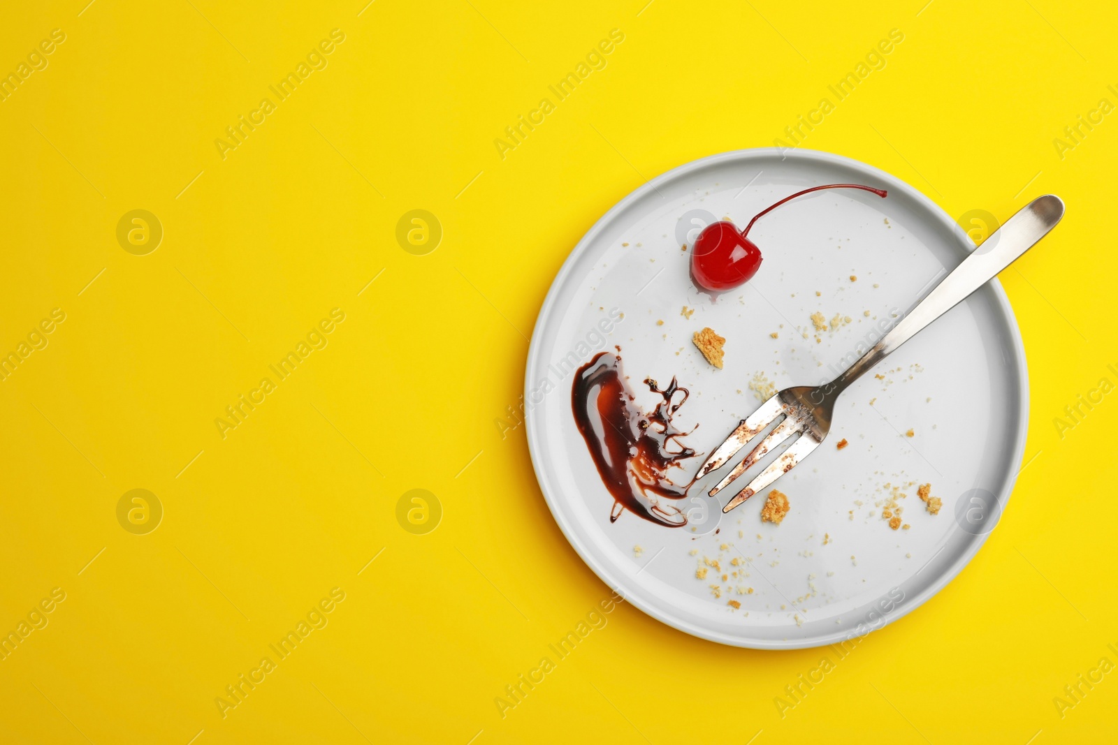 Photo of Dirty plate with food leftovers, fork and canned cherry on yellow background, top view. Space for text