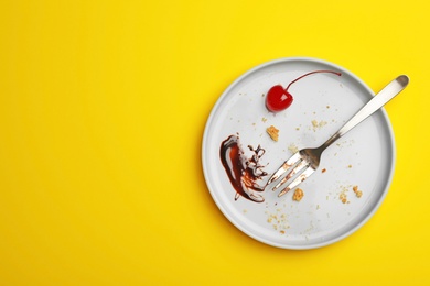 Photo of Dirty plate with food leftovers, fork and canned cherry on yellow background, top view. Space for text