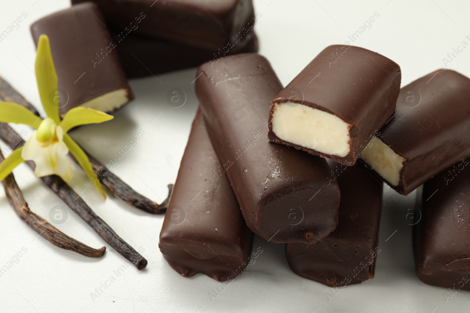 Photo of Glazed curd cheese bars, vanilla pods and flower on white table, closeup