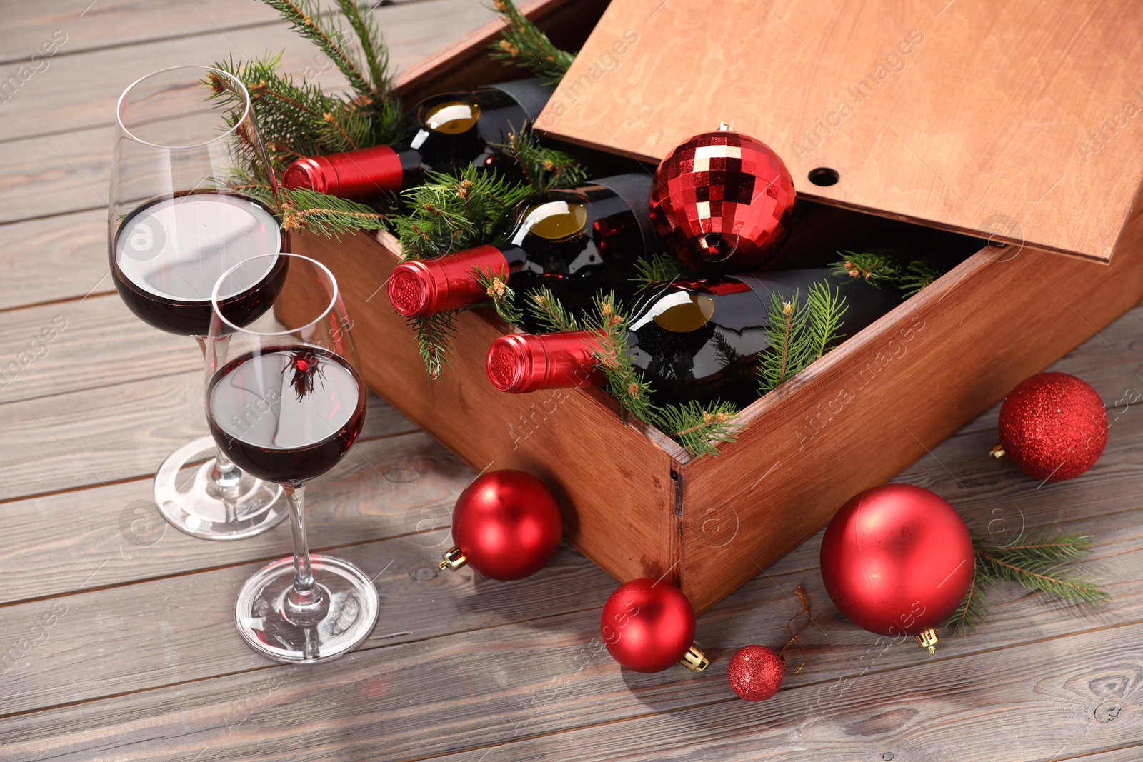 Photo of Wooden crate with bottles of wine, glasses, fir twigs and red Christmas balls on table