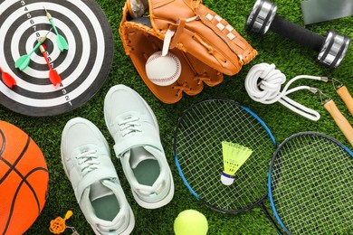 Photo of Different sport equipment and sneakers on green grass, flat lay