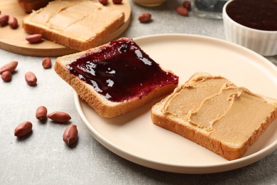 Photo of Tasty peanut butter sandwiches with jam and peanuts on gray table, closeup