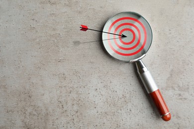 Image of Magnifying glass with illustration of target and arrow on grey textured background, top view. Space for text