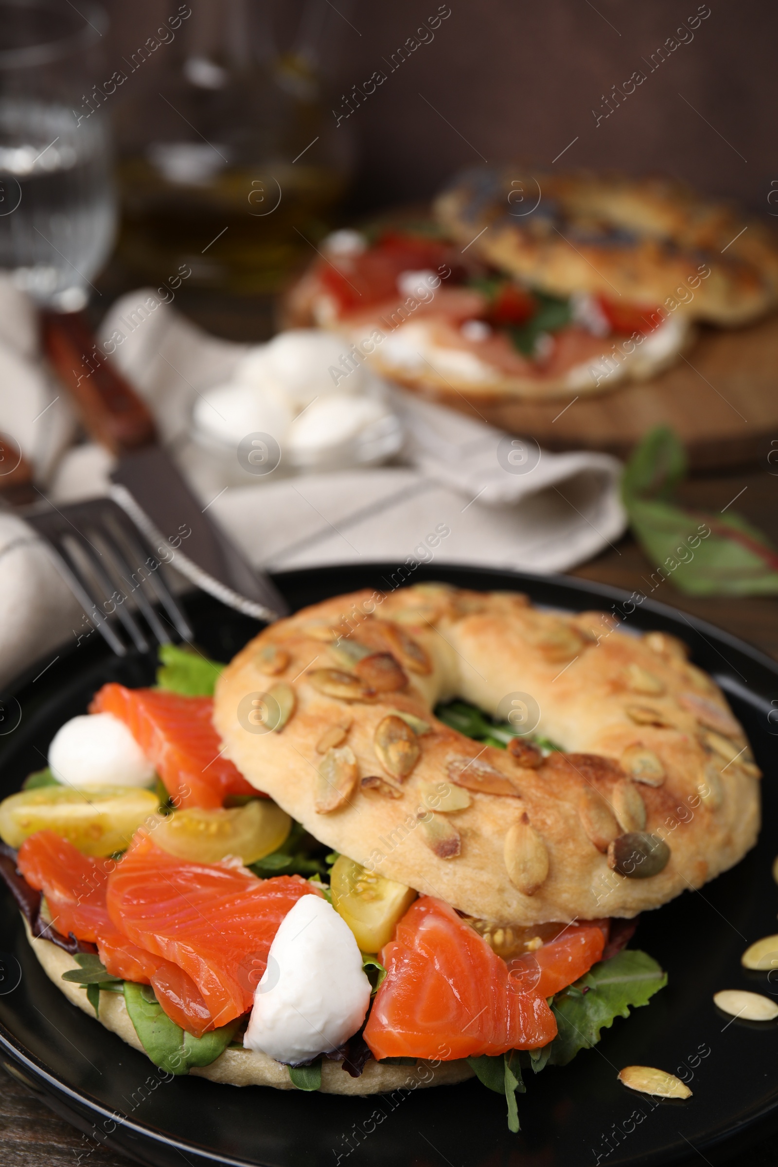 Photo of Tasty bagel with salmon, mozzarella cheese, tomatoes and lettuce on table