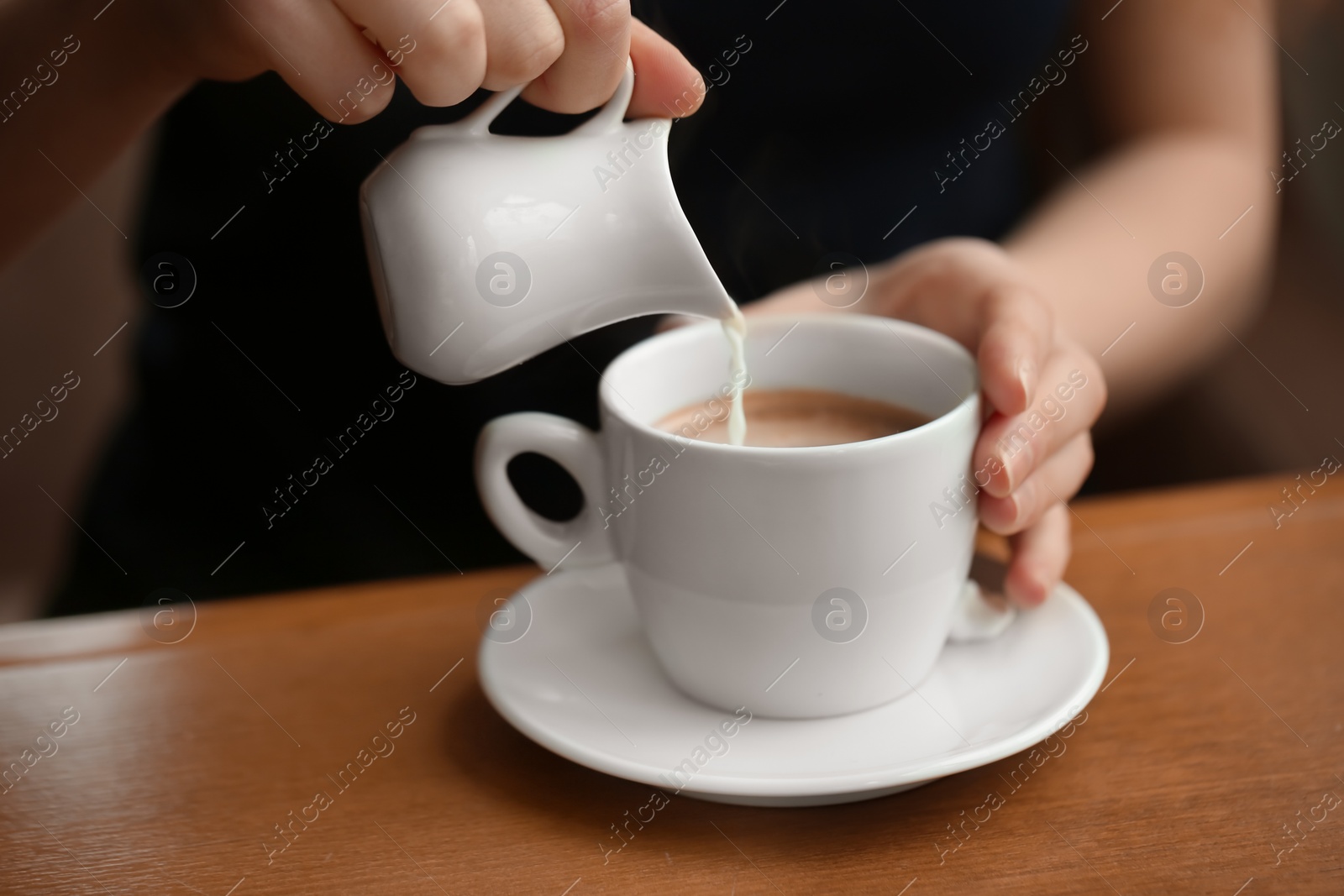 Photo of Woman pouring milk into cup of coffee on table