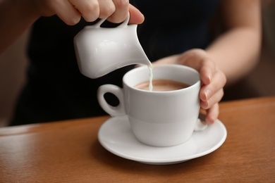 Photo of Woman pouring milk into cup of coffee on table