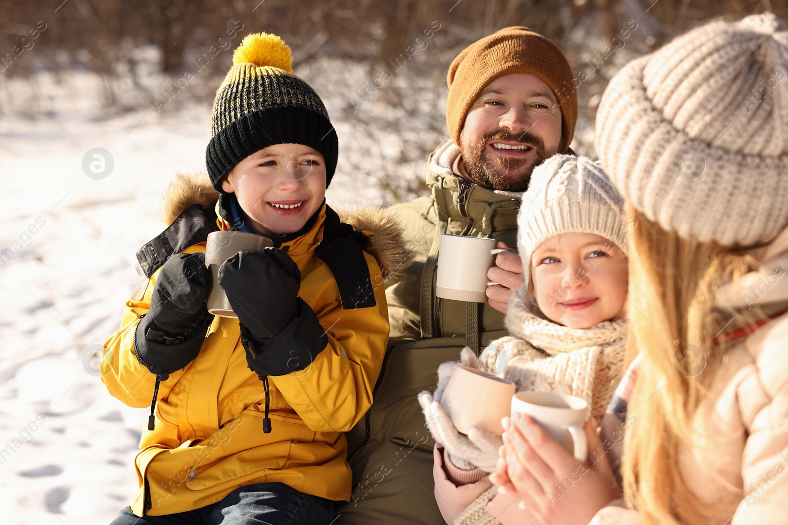 Photo of Happy family warming themselves with hot tea outdoors on snowy day