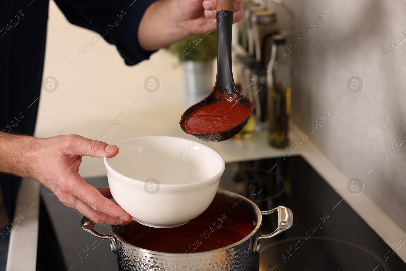 Photo of Man pouring delicious tomato soup into bowl in kitchen, closeup