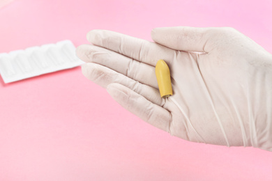 Photo of Woman holding suppository on pink background, closeup. Hemorrhoid treatment