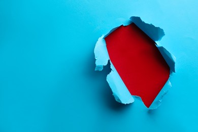 Photo of Hole in light blue paper on red background, space for text