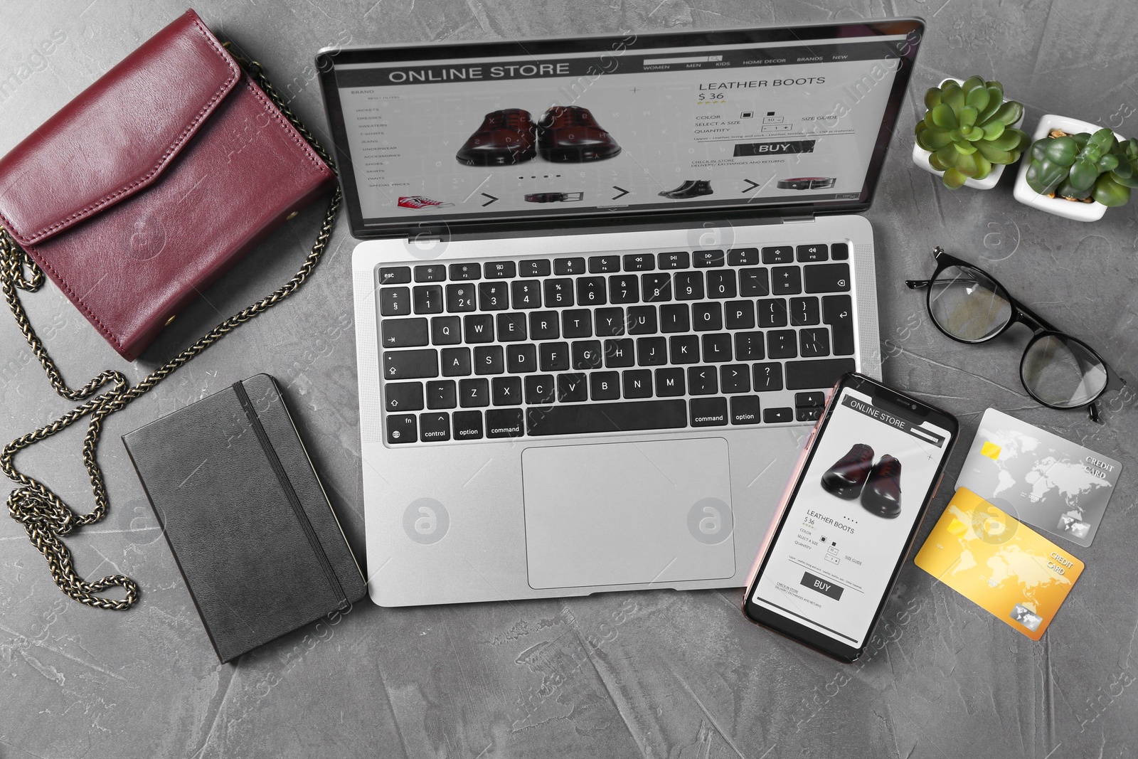 Photo of Online store website on laptop screen. Computer, smartphone, credit cards, notebook, accessories and houseplants on grey table, flat lay