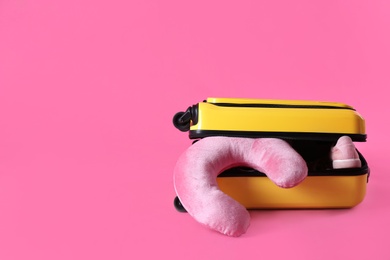 Yellow suitcase and travel pillow on pink background, space for text