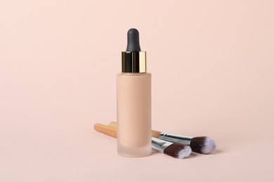 Photo of Bottle of skin foundation and brushes on beige background. Makeup product