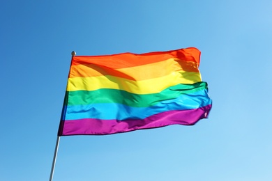 Photo of Rainbow LGBT flag fluttering on blue sky background. Gay rights movement