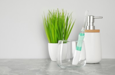 Electric toothbrush in glass, soap dispenser and green houseplant on light grey marble table. Space for text