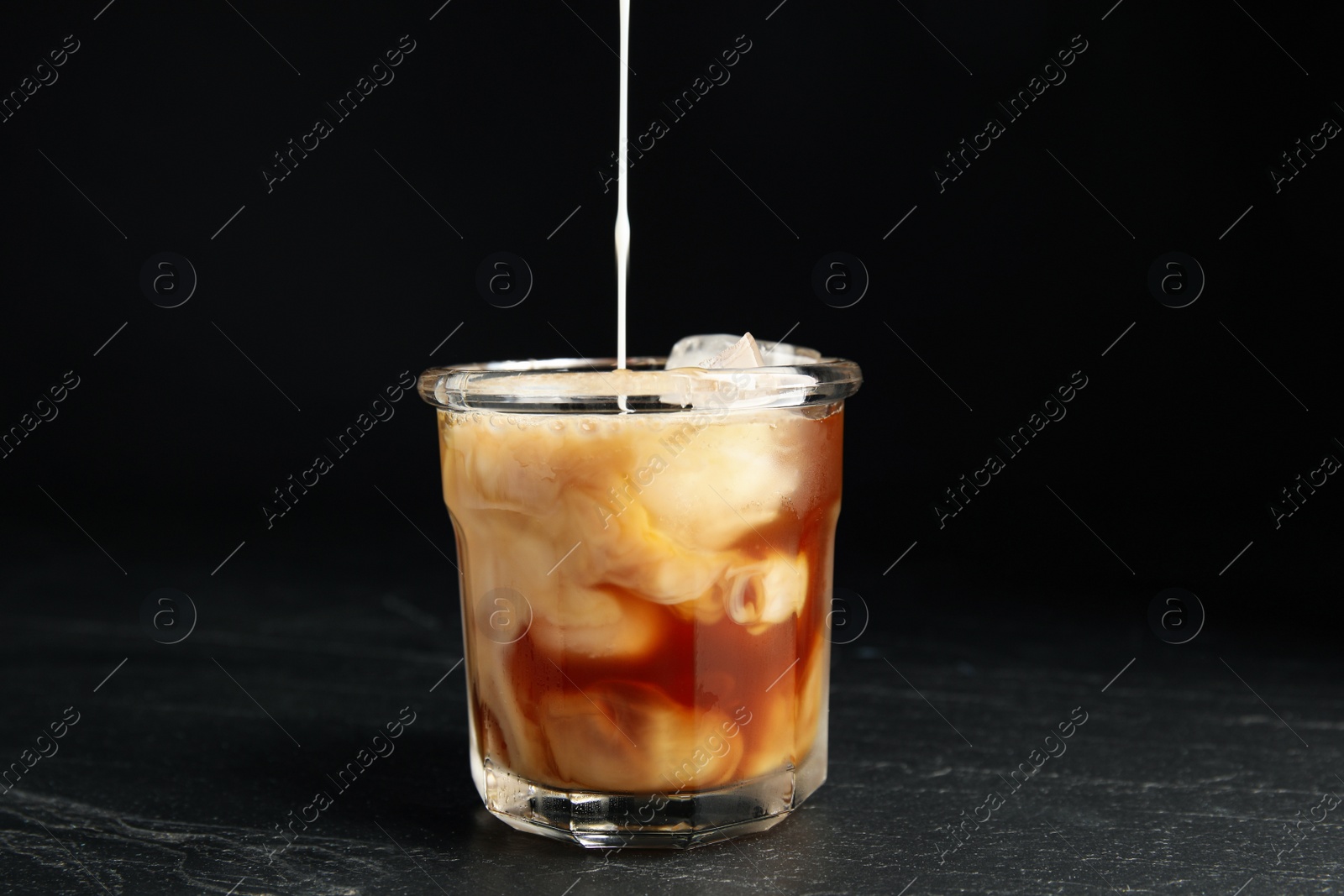 Photo of Pouring milk into glass with coffee on black table