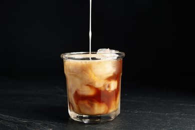 Pouring milk into glass with coffee on black table