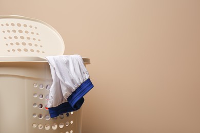 Plastic laundry basket with clothes on beige background. Space for text