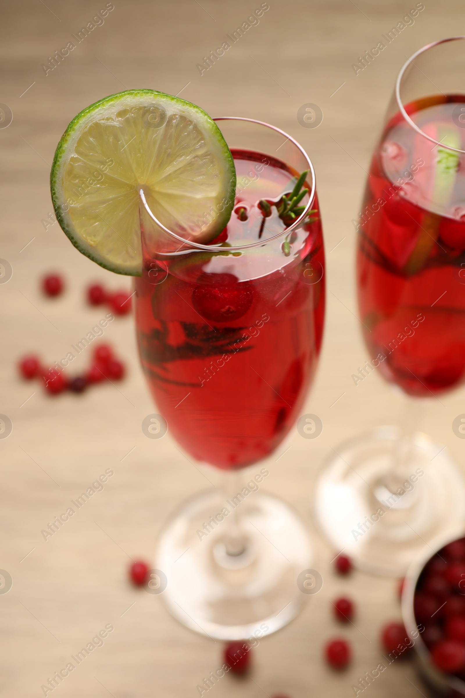 Photo of Tasty cranberry cocktail with rosemary and lime in glasses on beige table, closeup