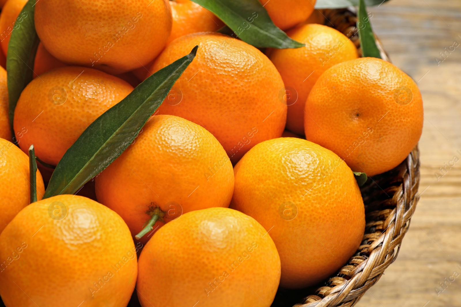 Photo of Fresh ripe tangerines with leaves in wicker basket, closeup. Citrus fruit