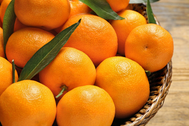 Fresh ripe tangerines with leaves in wicker basket, closeup. Citrus fruit