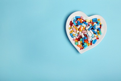 Heart shaped plate with different pills on color background. Cardiology concept