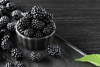 Fresh ripe blackberries and leaf on black wooden table. Space for text