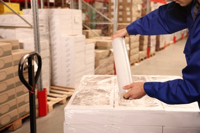 Photo of Worker wrapping boxes in stretch film at warehouse, closeup
