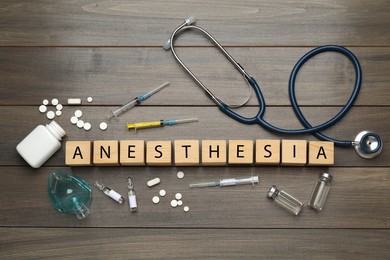 Flat lay composition with word Anesthesia made of cubes and drugs on wooden table