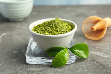 Bowl with matcha tea and green leaves on table