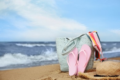 Photo of Bag and different beach objects on sand near sea, space for text