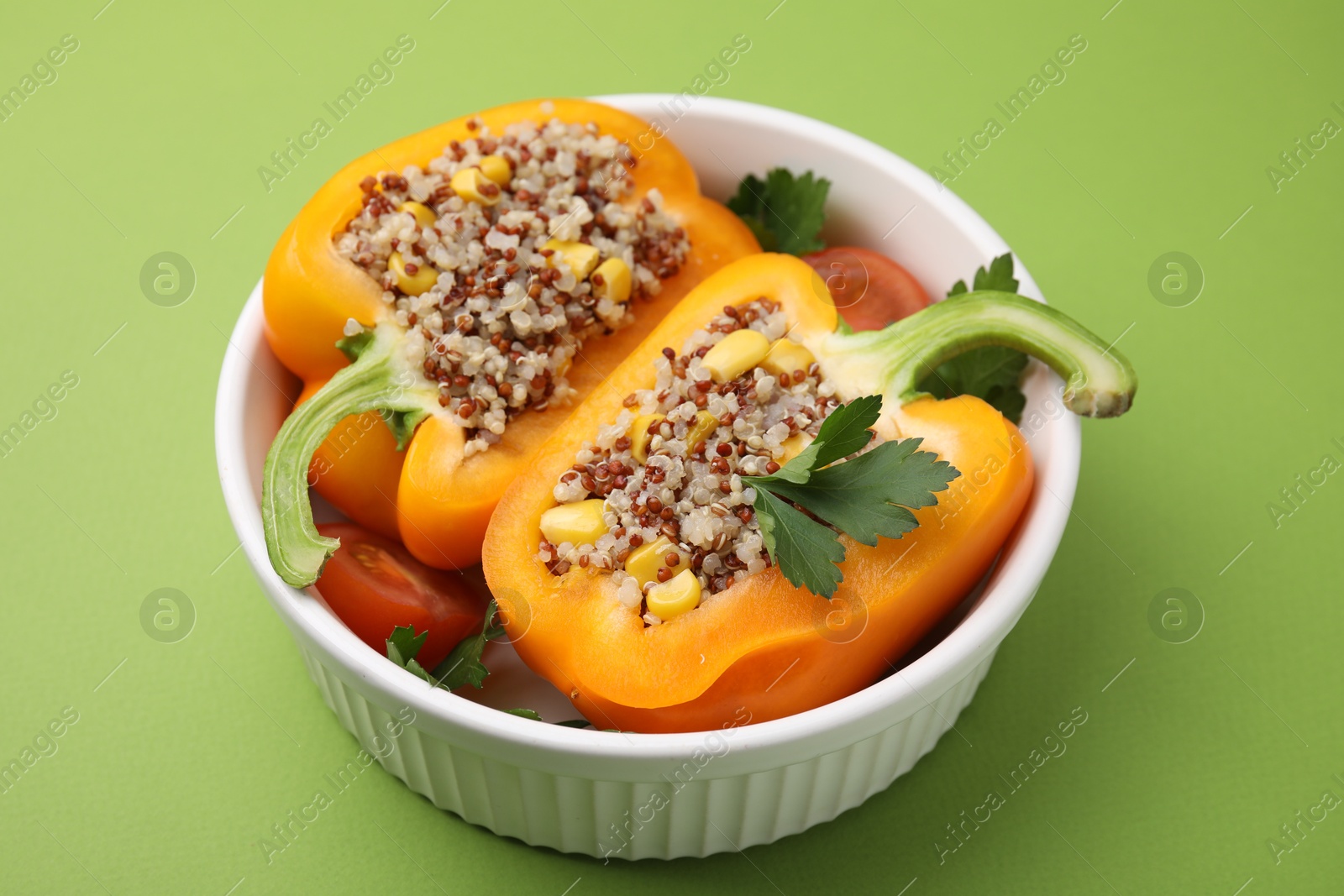 Photo of Quinoa stuffed bell pepper and parsley in bowl on green background, closeup