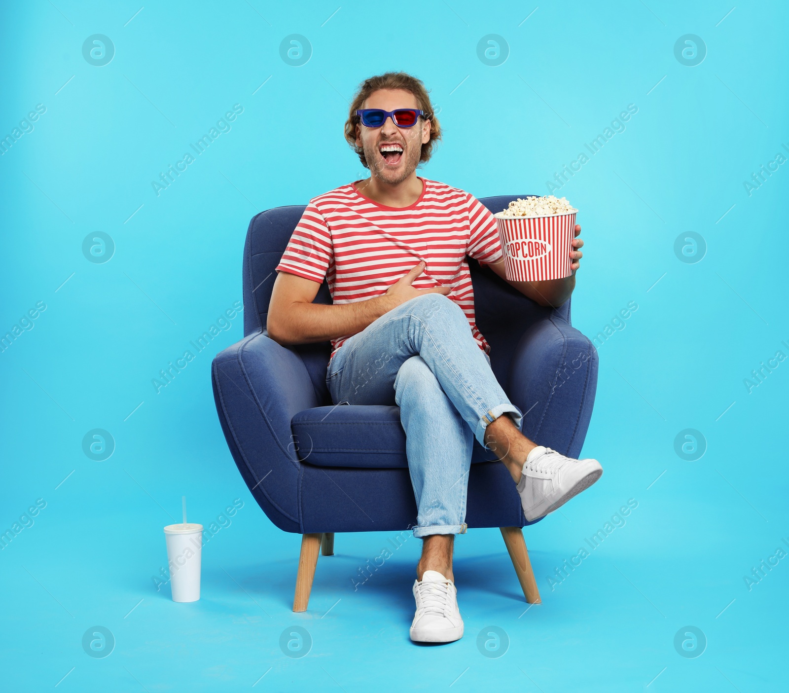 Photo of Man with 3D glasses, popcorn and beverage sitting in armchair during cinema show on color background