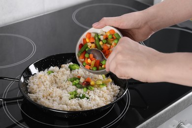 Photo of Woman cooking tasty rice with vegetables on induction stove, closeup