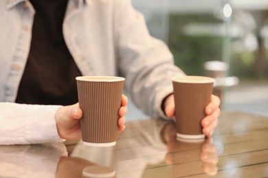 Photo of Women holding takeaway paper cups at table, closeup. Coffee to go