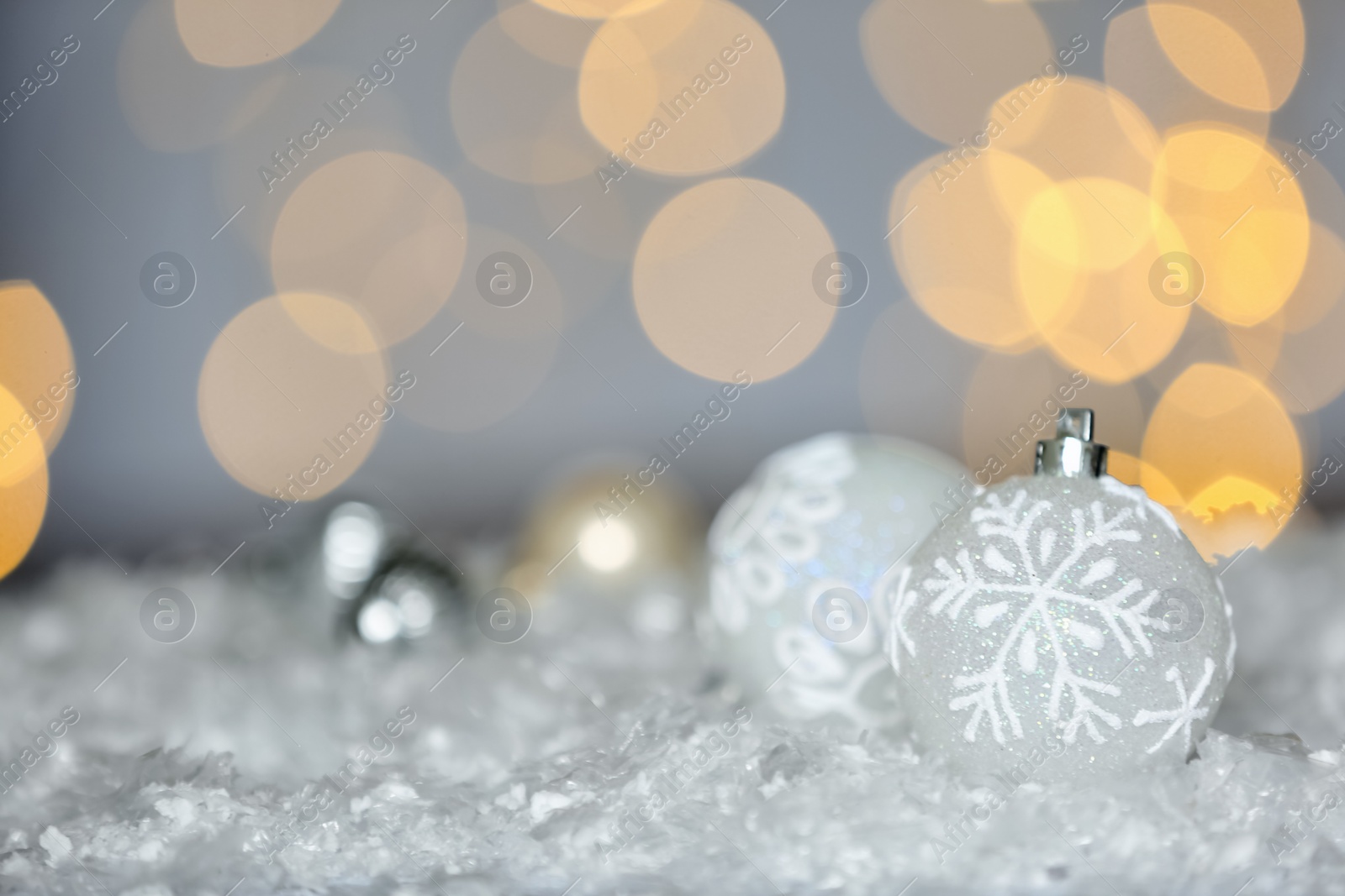 Photo of Beautiful white Christmas balls on snow against blurred festive lights, space for text